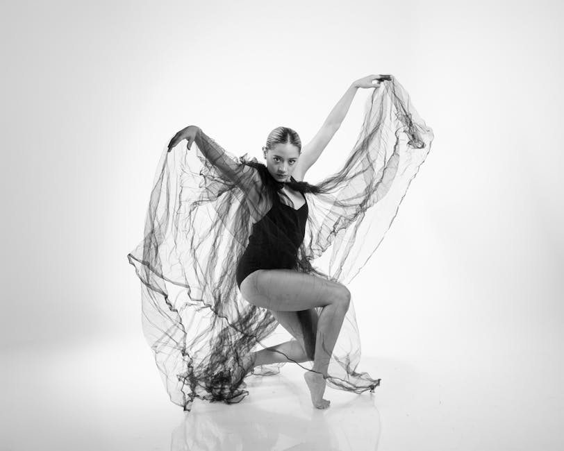 Artistic black and white portrait of a female dancer in a dynamic pose with flowing fabric.